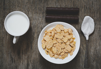 Breakfast cereal wheat flakes in bowl with milk on wooden table