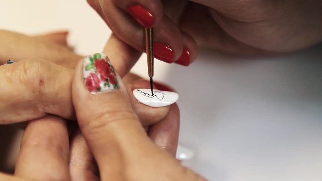 Cosmetic salon manicure session, woman hand painting heart pattern on white nail polish, close up