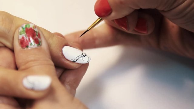 Beauty shop manicure session, woman hand painting heart picture on white nail polish, close up