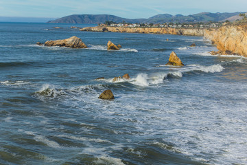 Waves crash in a blue ocean against rocky outcrops along Pismo Beach