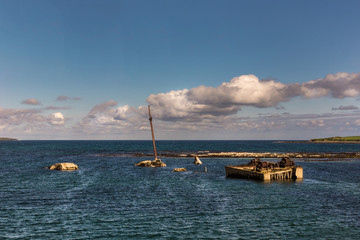 Orkneys, Scotland - June 5, 2012: The mast and other rusty parts of WW II warship wreck peep out of the sea near Lamb Holm Island. Atlantic Ocean is the horizon. Blue water, blue cloudy skies.