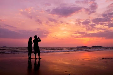Photo sur Plexiglas Mer / coucher de soleil Silhouette of romantic couple standing on the beach at sunset