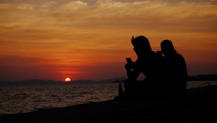 Fototapeta na wymiar Men and Women Sitting on the beach Watching the sunset. Twilight sky background