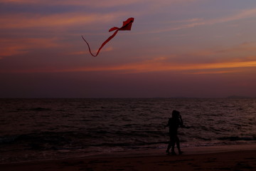 Boy and girl playing a kite on the beach. Twilight sky background.