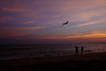 Boy and girl playing a kite on the beach. Twilight sky background.