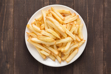 French fries on white dish on wooden background.