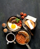 breakfast in a frying pan, fried eggs, sausages and tomatoes on a dark background