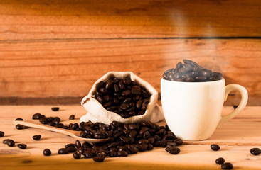 the coffee beans and cup of coffee with smoke on wooden table background