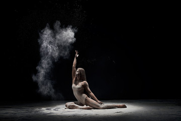 Graceful girl posing in white dust cloud in studio