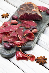 Whole-muscle cuts of meat are shaved into slices. Sliced smoked beef. Charcuterie. Homemade dried meat sliced and served with olives.