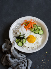 Rice with fried egg, pickled carrots, cucumber and seaweed. Healthy diet food concept. Top view, on a dark background