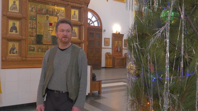 a Bearded Man Looks at a Decorated Tree in Church, With Impressive Old Icons Hanging on the Walls of an Old Orthodox Temple