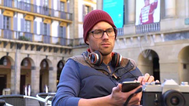 Hipster guy relaxing at terrace, using smartphone