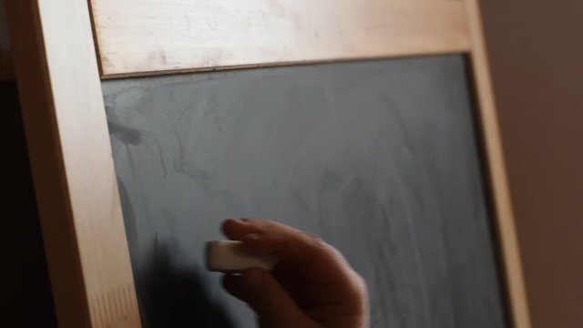 Young girl writing on a chalkboard with a piece of chalk. Close Up.
