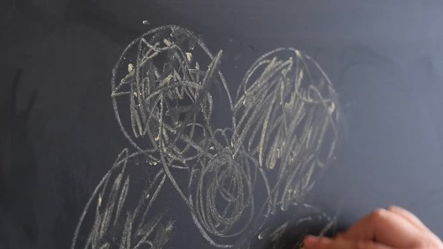 Young girl drawing on a chalkboard with a piece of chalk. Close Up.
