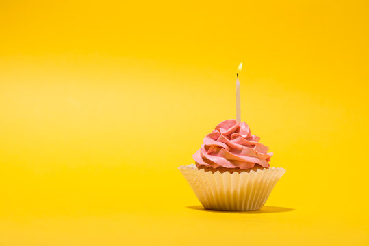 Birthday cupcake with  candle on yellow background.
