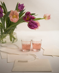 Pink tulips in a clear vase and two glasses of juice on a table with letters and envelopes