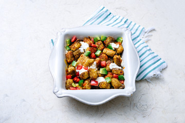 Overhead of tater tot southwestern casserole topped with fresh avocado, tomatoes, and dollops of rich sour cream in square, Southern casserole dish on turquoise striped linen on cream marble surface.