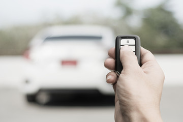 Hand of man holding and push remote control of car and white car parking background technology transportation safety concept