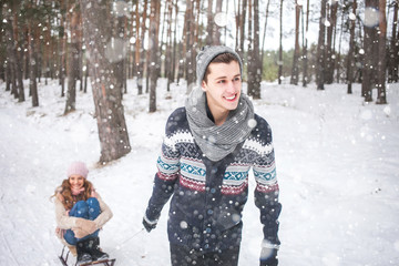 Young couple walking and sledding in the winter in the forest during a snowfall