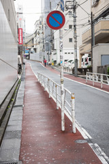 A walking pathway is seen on the picture with railings on both side of the road. High rise buildings are seen on both the sides of the road. A pedestrian is also seen walking.