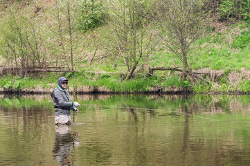 Fototapeta na wymiar Fisherman fishing on a small spring river. Fly fishing.