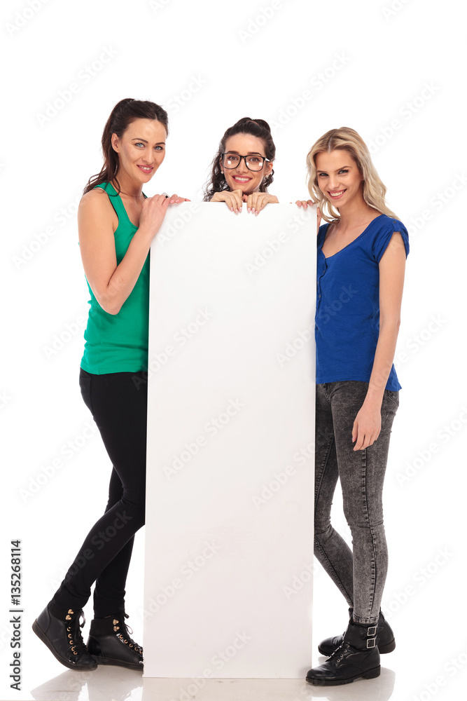 Poster three happy casual women presenting a big blank board