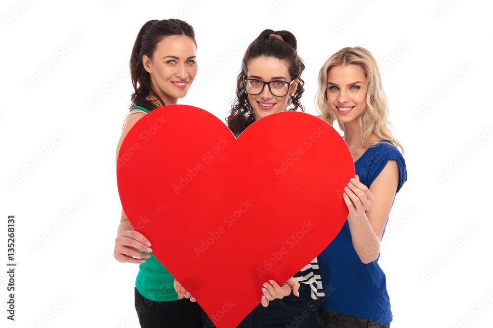 Sticker three smiling casual women holding a big red heart