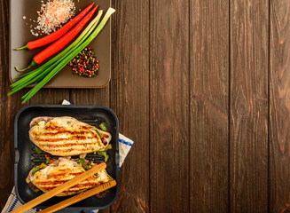 The juicy chicken fillet and vegetables made on a grill on a brown wooden background. Flat lay,...