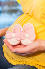 беременная женщина держит розово-белые пинетки в руках
