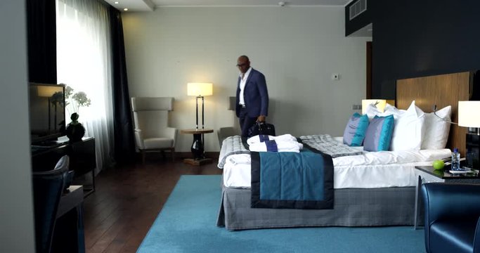 Comfortable Hotel Room for a Businessman/Afro-american businessman enters the hotel room. He carries a laptop and a suitcase