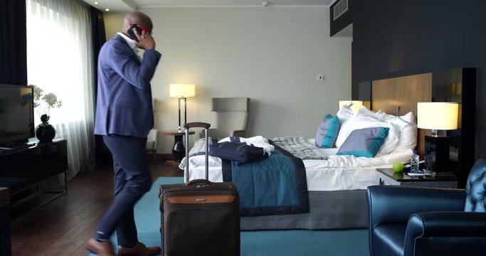 The Business Call in a Hotel Room/Afro-american businessman walks around the hotel room while talking on the phone
