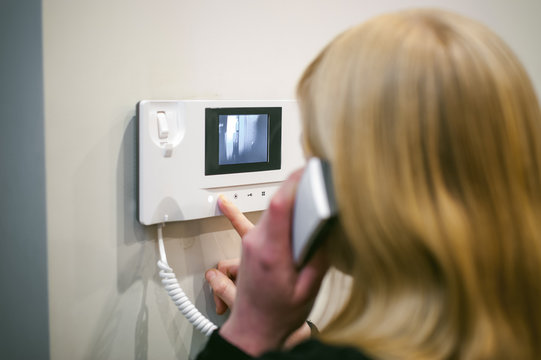 blonde woman hangs up the phone after answering the intercom call in her apartment