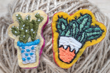 Two cactuses in pots, hand-made embroidery in the form of brooches, on the background of the thread ball