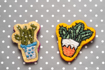 Two cactuses in pots, hand-made embroidery in the form of brooches, on dots paper with copy space