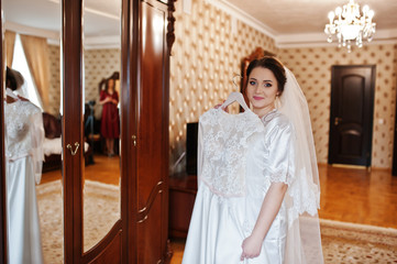 Cute brunette bride on silk robe with wedding dress on hands.