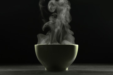 A bowl of hot food and steam on dark background.