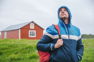 Tourist with a backpack in  blue jacket on  background of green field
