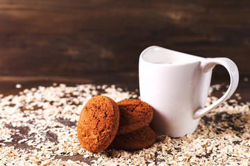Oatmeal cookies on a background of oats, next to a glass of milk, on vintage board