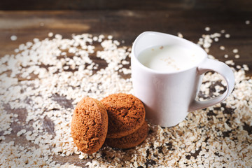 Oatmeal cookies on a background of oats, next to a glass of milk, on vintage board