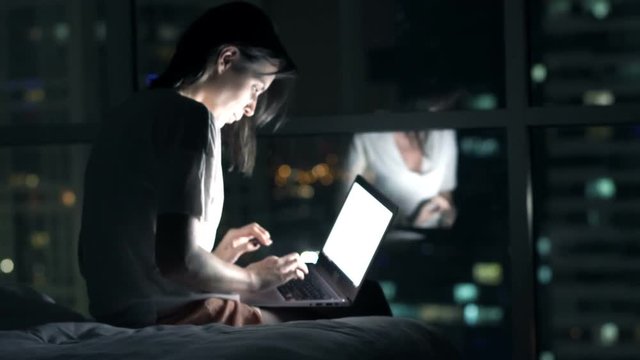 Young woman finish working on laptop and falling asleep in bedroom at night
