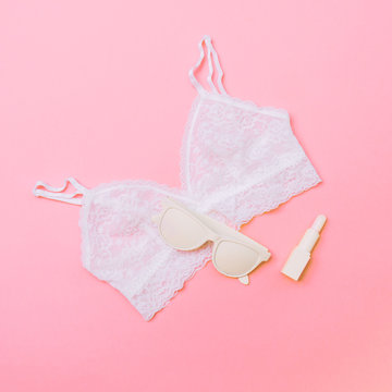 white sunglasses, lipstick and lace underwear bra on pink background. minimal fashion concept.