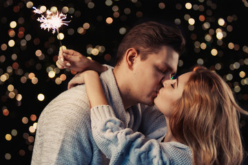 Cheerful couple in winter clothes hugging and kissing. Low light