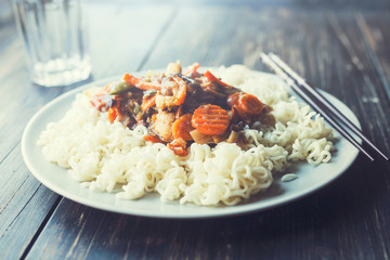 Plate of noodles and stir fry vegetables, with chopsticks and glass of water in background