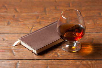 Glass of cognac, notebook on wooden background