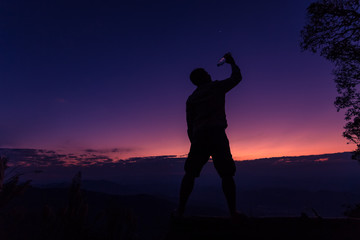 Silhouette of a man drinking happily at sunset.