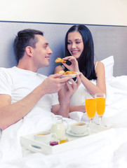 Fototapeta premium smiling couple having breakfast in bed in hotel