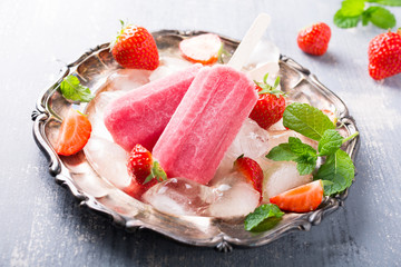 Homemade strawberry popsicles on metal plate with ice and berries. Summer food concept.