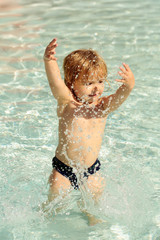 Cute baby boy sprinkles water in outdoor pool