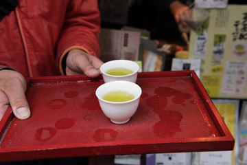 In the picture we can see a man holding a tray with two cups to serve hot green tea. Green tea is very popular in Japan.